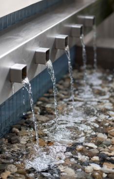 "This is a deceptive little water feature," says Kate Wiseman. "It doesn't look as hard to build as it actually is." To get the water to fall evenly from all five spouts is a physical challenge, she explains. To overcome this issue, she collaborated with the general contractor and they both came up with the idea to build a reservoir behind the spouts so that it would fill up with water first and then spill out all of the spouts simultaneously.