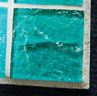 These tiles show cracks and stresses purposely induced in a manufacturer’s lab for testing. The black glass shows internal stress caused by the incorporation of incompatible raw materials. In the green tile, a thermal-shock crack developed when staff brought the tile to a high temperature, then soaked it in cold water. On an actual installation, these cracks generally are clean and run all the way through the tile. The purple glass has experienced a strain during annealing, a process by which cooling is controlled. Each glass formula has its own annealing point, which must be observed to avoid these stresses.